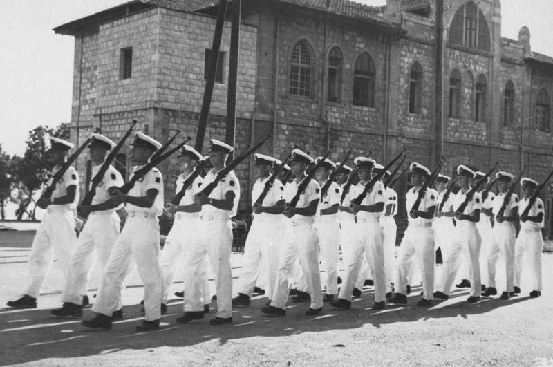 הקדטים צועדים בבית הספר לקציני ים בעכו על רקע בנין תחנת הרכבת הטורקית 